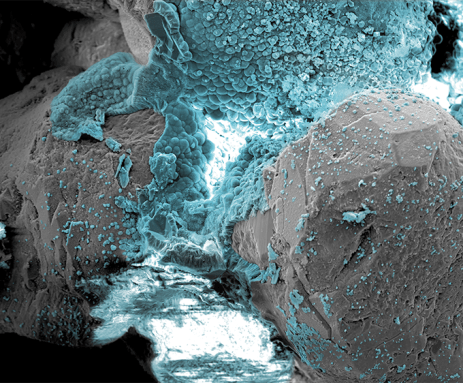 Blue bubbly material fills the middle and top of this microscopy image. It shows the minerals created when sand is zapped with low voltage electricity in an effort to sand into stone.